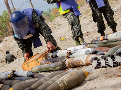 A person in a HALO vest and visor carefully handling a box among a stockpile of weapons in Honduras